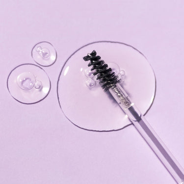 Droplets of Madara Brow & Lash Booster with the applicator brush lying beside them