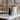 A black bottle of INLIGHT Night Repair Serum sits on a white marble countertop in a bathroom setting with a blurred stone wall and brass fixtures in the background.