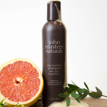Bottle of John Masters Daily Nourishing Shampoo With Citrus & Geranium with plants in background