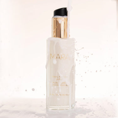 Open bottle of Mara Pearl Peptide Glaze Facial Essence on white shelf and white liquid splashed around bottle to show texture