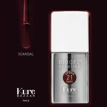 A bottle of Kure Bazaar Paris Biogel Keratine nail polish in the shade Scandal, shown next to a brush with deep burgundy polish on a dark, reflective background.